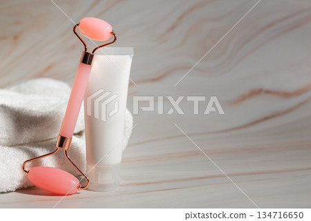 Beauty facial roller and blank cosmetic tube on soft towel with marble background, skincare product mockup for spa, wellness, self-care, anti-aging rituals and modern beauty branding. 134716650
