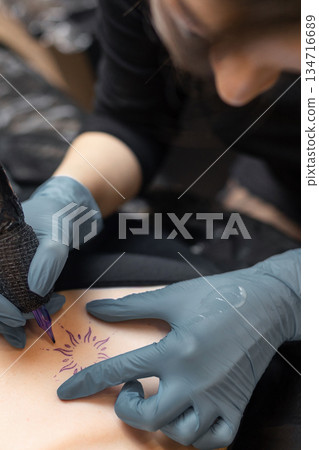 tattoo artist working on a woman chest design in a studio, showing the process of professional tattooing, precision, sterile gloves and cosmetic procedure atmosphere. tattoo artist working on a woman chest design in a studio, showing the process of professional tattooing, precision, sterile gloves and cosmetic procedure atmosphere. 134716689
