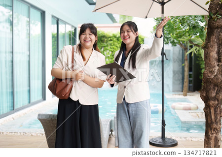 Real Estate Agents. Two women showcasing a property with a pool in a modern setting. Real Estate Agents. Two women showcasing a property with a pool in a modern setting. 134717821