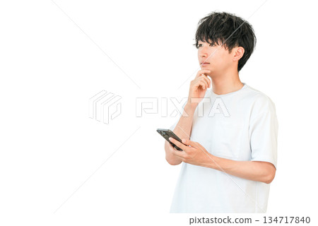 A young Asian man thinking, considering, worrying while looking at his smartphone 134717840