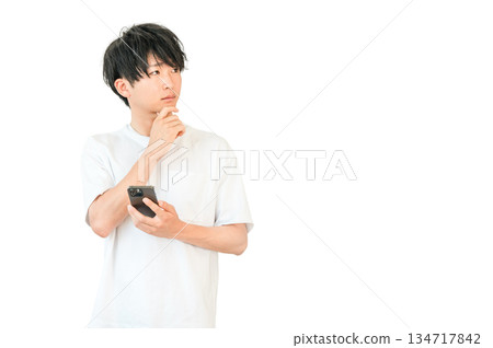一位年輕的亞洲男子一邊看著智慧型手機，一邊思考、考慮、擔憂 134717842