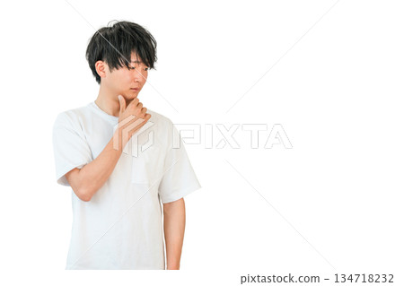 一位年輕的亞洲男子托著下巴,低頭看著地面(思考、考慮、擔憂、後悔、不滿、不信任)。 一位年輕的亞洲男子托著下巴,低頭看著地面(思考、考慮、擔憂、後悔、不滿、不信任)。 134718232