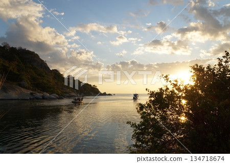 A colorful wooden boat sets out to sea at dawn to fish. It's morning, dawn, and hot. In the background is a mountain with green trees and grass and a blue sky. A colorful wooden boat sets out to sea at dawn to fish. It's morning, dawn, and hot. In the background is a mountain with green trees and grass and a blue sky. 134718674