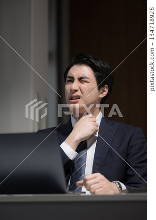 A businessman with a sore throat and a cold who has been working overtime in front of a computer in a dark office without finishing his work A businessman with a sore throat and a cold who has been working overtime in front of a computer in a dark office without finishing his work 134718928