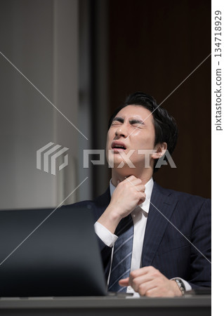 A businessman with a sore throat and a cold who has been working overtime in front of a computer in a dark office without finishing his work A businessman with a sore throat and a cold who has been working overtime in front of a computer in a dark office without finishing his work 134718929