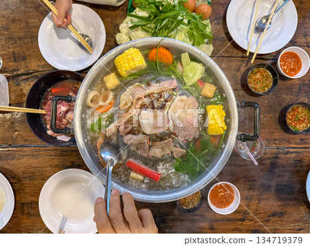 Sliced meat and vegetables cook in a metal grill pot filled with broth and steam, while the center grill browns the meat. 134719379
