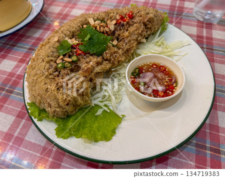Thai crispy fish salad Yum pla duk foo is served fresh and crispy with herbs and dipping sauce, ready to eat at the table. 134719383