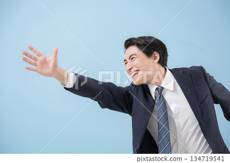 Close-up of a jumping, dynamic businessman in a suit reaching out to grasp his goal or future, light blue background Close-up of a jumping, dynamic businessman in a suit reaching out to grasp his goal or future, light blue background 134719541