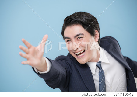 特寫鏡頭：一位身穿西裝、充滿活力的商人躍起，伸手去抓住他的目標或未來，背景為淺藍色。 134719542