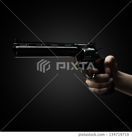 Human hand holding a revolver handgun against a dark background. Concept of gun violence 134719719