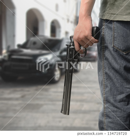 Man hand holding a revolver handgun in a blurred city street scene, suggesting crime, danger, and a tense situation. Concept of gun violence 134719720