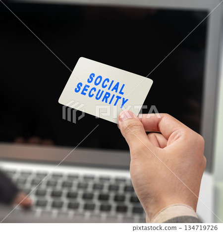 Human hand holding a card with the words of Social Security against a blurred laptop screen. Mockup, Copy space, or template. Concept of Social Security 134719726