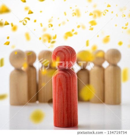 Wooden figure in red standing out from a crowd of beige figures, emphasized by falling yellow confetti. Concept of Winner 134719734