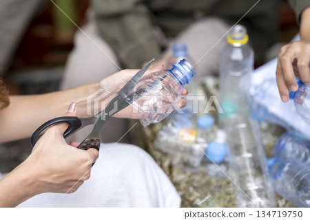 People gathered outdoors, actively participating in a recycling initiative. Decorating with plastic bottles promotes environmental sustainability. Spirit of eco-consciousness 134719750