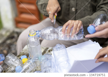 People gathered outdoors, actively participating in a recycling initiative. Decorating with plastic bottles promotes environmental sustainability. Spirit of eco-consciousness People gathered outdoors, actively participating in a recycling initiative. Decorating with plastic bottles promotes environmental sustainability. Spirit of eco-consciousness 134719751
