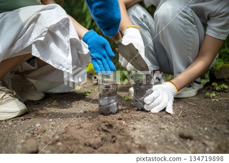 Women are shown planting a garden inside a recycled plastic bottle, showcasing environmental awareness and sustainable practices outdoors 134719898