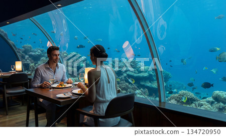 Couple enjoys romantic aquarium dinner date. Underwater aquarium restaurant with coral reef view, aquarium mood for valentines day, anniversary dining, luxury travel concept, soft candlelight 134720950