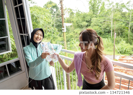 Two Indonesian southeast asian women wearing sportswear and a towel around neck is holding a water bottle after a workout. She appears refreshed and healthy Two Indonesian southeast asian women wearing sportswear and a towel around neck is holding a water bottle after a workout. She appears refreshed and healthy 134721346