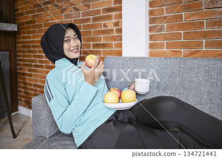Indonesian southeast asian woman is enjoying a fruit indoors after a workout. Eating a healthy meal and smiling Indonesian southeast asian woman is enjoying a fruit indoors after a workout. Eating a healthy meal and smiling 134721441