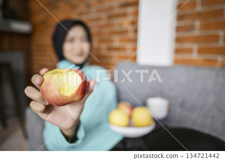 Indonesian southeast asian woman is enjoying a fruit indoors after a workout. Eating a healthy meal and smiling Indonesian southeast asian woman is enjoying a fruit indoors after a workout. Eating a healthy meal and smiling 134721442