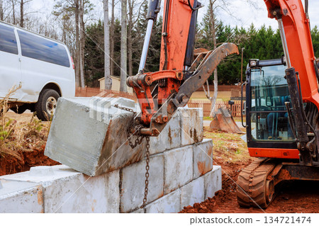 Excavator lifts concrete block from ground places it on retaining walls during construction site 134721474