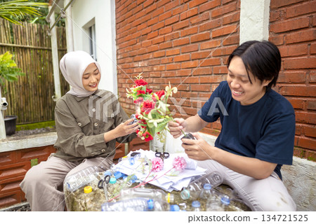 Indonesian southeast asian people gathered outdoors, actively participating in a recycling initiative. Decorating with plastic bottles promotes environmental sustainability. Spirit of 134721525