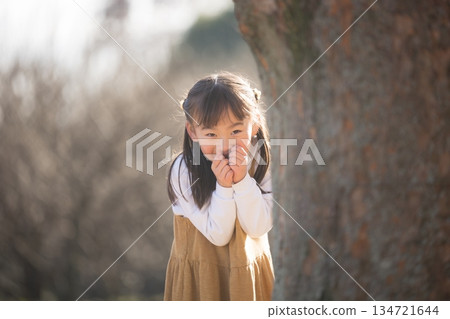 A girl peeking out from behind a tree, playing traditional games like hide-and-seek and Daruma-san koronda in the park 134721644