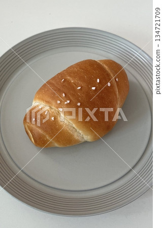 Golden brown salt bread with a soft, fluffy interior and a perfectly crisp crust, lightly sprinkled with coarse salt for a savory touch. A simple yet satisfying treat for any occasion. 134721709