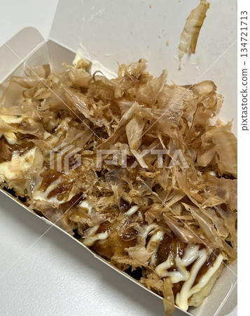 Takoyaki, a popular Japanese street food, are crispy round dough balls filled with octopus, tempura bits, and pickled ginger, topped with takoyaki sauce, bonito flakes, and aonori. 134721713