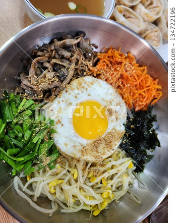 Bibimbap, a vibrant Korean rice dish topped with a variety of seasoned vegetables, gochujang, and a fried egg, often accompanied by sliced meat. Mixed together, it creates a flavorful and balanced. Bibimbap, a vibrant Korean rice dish topped with a variety of seasoned vegetables, gochujang, and a fried egg, often accompanied by sliced meat. Mixed together, it creates a flavorful and balanced. 134722196