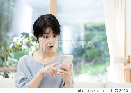 Young woman sitting on sofa and using smartphone Young woman sitting on sofa and using smartphone 134722460