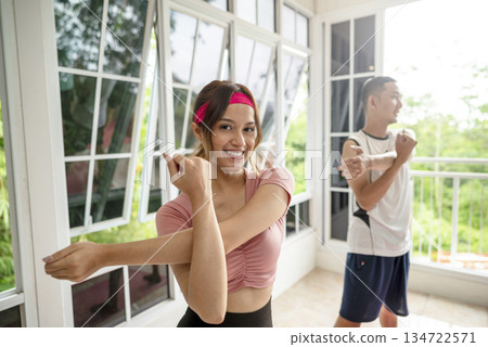 Indonesian southeast asian people perform a stretching routine together in a bright, airy indoor space with large windows. Health, fitness, and togetherness Indonesian southeast asian people perform a stretching routine together in a bright, airy indoor space with large windows. Health, fitness, and togetherness 134722571