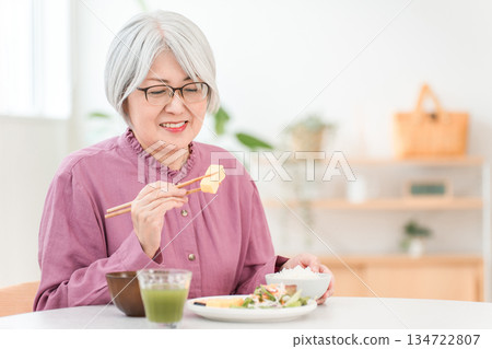 一位頭髮花白的老婦人在家裡的餐廳吃飯。 一位頭髮花白的老婦人在家裡的餐廳吃飯。 134722807