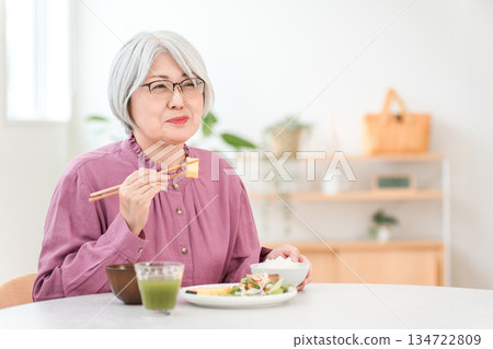 A gray-haired senior woman eating in the dining room at home 134722809