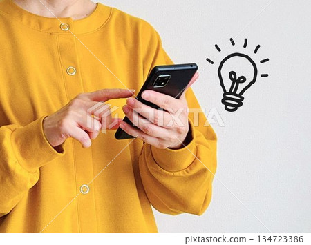 A woman operating a smartphone and a miniature light bulb 134723386