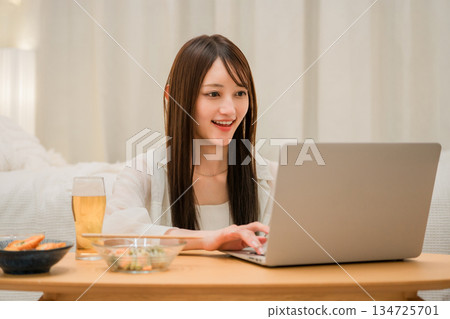 晚上在家吃飯時,年輕的亞洲女性一邊放鬆一邊看筆記型電腦 晚上在家吃飯時,年輕的亞洲女性一邊放鬆一邊看筆記型電腦 134725701