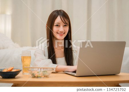 Young Asian woman relaxing and looking at laptop while eating at home in the evening 134725702