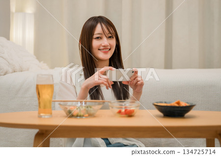 一位年輕的亞洲女性在家裡的臥室裡一邊喝啤酒一邊看智慧型手機(啤酒,在家喝酒,飲酒習慣) 一位年輕的亞洲女性在家裡的臥室裡一邊喝啤酒一邊看智慧型手機(啤酒,在家喝酒,飲酒習慣) 134725714