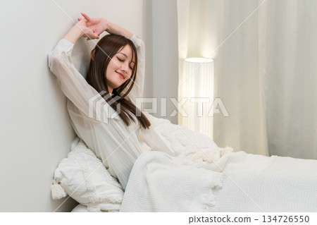 A woman stretching in her bedroom in the morning after a good night's sleep A woman stretching in her bedroom in the morning after a good night's sleep 134726550