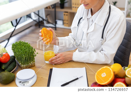 A doctor in a white coat squeezes fresh orange juice into a glass, surrounded by healthy food options. A doctor in a white coat squeezes fresh orange juice into a glass, surrounded by healthy food options. 134726937