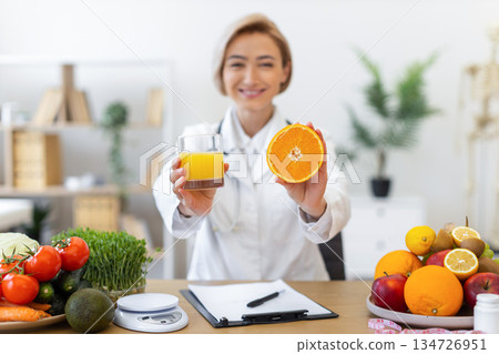 A nutritionist holds up a glass of juice and a sliced orange, promoting healthy eating and nutrition. 134726951