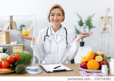 A smiling nutritionist presents two glasses, one with juice and the other with water, promoting healthy eating and lifestyle choices. 134726962