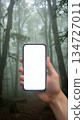 Mockup image of a hand holding mobile phone with white screen over forest background 134727011