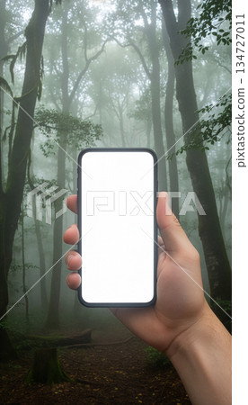 Mockup image of a hand holding mobile phone with white screen over forest background 134727011