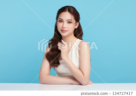 A beautiful young Asian woman with clean, fresh skin against a blue background. Skincare, facial treatment, cosmetology, beauty, and spa. An elegant portrait of an Asian woman. A beautiful young Asian woman with clean, fresh skin against a blue background. Skincare, facial treatment, cosmetology, beauty, and spa. An elegant portrait of an Asian woman. 134727417