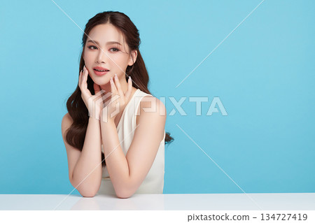 A beautiful young Asian woman with clean, fresh skin against a blue background. Skincare, facial treatment, cosmetology, beauty, and spa. An elegant portrait of an Asian woman. 134727419
