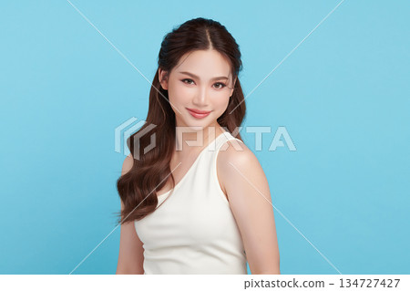 A beautiful young Asian woman with clean, fresh skin against a blue background. Skincare, facial treatment, cosmetology, beauty, and spa. An elegant portrait of an Asian woman. 134727427