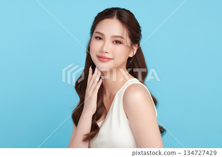 A beautiful young Asian woman with clean, fresh skin against a blue background. Skincare, facial treatment, cosmetology, beauty, and spa. An elegant portrait of an Asian woman. A beautiful young Asian woman with clean, fresh skin against a blue background. Skincare, facial treatment, cosmetology, beauty, and spa. An elegant portrait of an Asian woman. 134727429