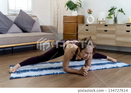 Asian woman in her 50s warms up on a yoga mat on the floor before starting 134727614