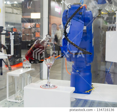 Robotic manipulators. Robot pouring liquid drink from bottle into glass. Industrial robot. Robot arm hand. Industrial manipulators for variety welding, material handling, palletizing. Robotization Robotic manipulators. Robot pouring liquid drink from bottle into glass. Industrial robot. Robot arm hand. Industrial manipulators for variety welding, material handling, palletizing. Robotization 134728136